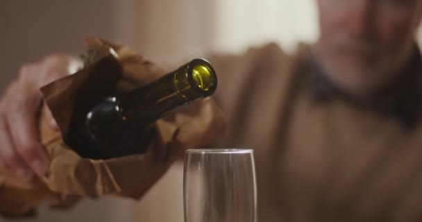 Un uomo dai capelli grigi versa il vino da una bottiglia in un bicchiere, primo piano — Video Stock