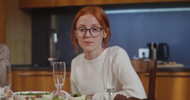 Ένα νεαρό κορίτσι χαμογελώντας κοιτάζει απευθείας στην κάμερα, κάθεται στο στρωμένο γιορτινό τραπέζι — Αρχείο Βίντεο