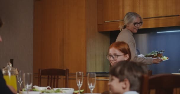 Een vrouw plaatst een geroosterde kalkoen in het midden van een feestelijk gedekte tafel — Stockvideo