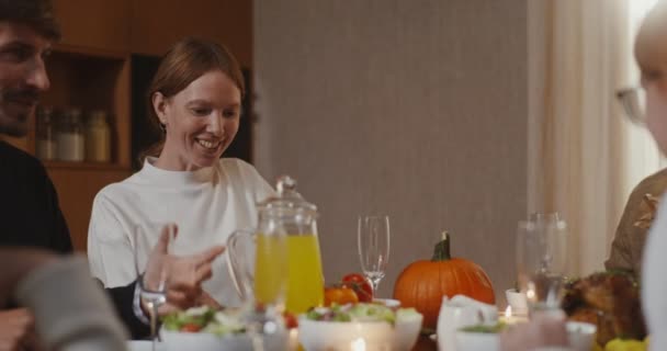 Рыжая женщина улыбается и болтает со своей семьей за праздничным столом — стоковое видео