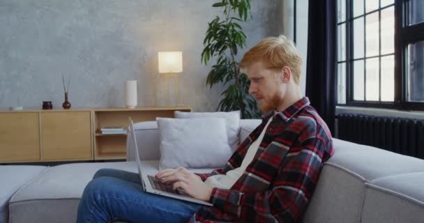 Ein junger Mann mit Bart beendet die Arbeit auf einem Laptop, gähnt und reibt sich die Augen — Stockvideo