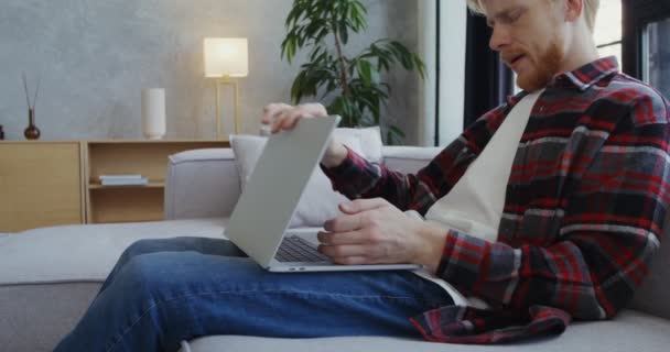 Ein junger Mann beendet seine Arbeit am Laptop, gähnt und nimmt ein Handy — Stockvideo