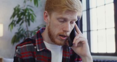 Sakallı genç bir adam cep telefonuyla ciddi ciddi konuşuyor..