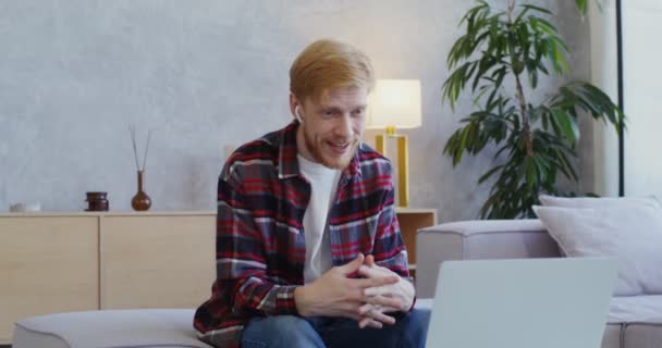 A man finishes video call on a laptop and takes out headphones with relief — Stock Video