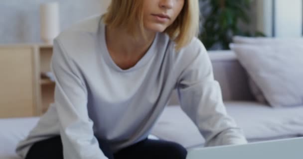 Uma jovem mulher sorrindo falando em videochamada no laptop enquanto se senta no sofá — Vídeo de Stock