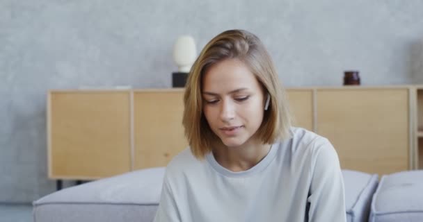 一个女人带着耳机在笔记本电脑上通过视频通话，喝着杯子里的水 — 图库视频影像