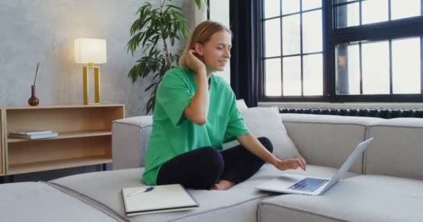 Une jeune femme souriante parlant sur appel vidéo sur un ordinateur portable alors qu'elle était assise sur un canapé — Video