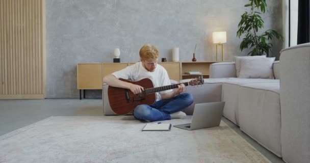Muž evropského vzhledu se naučí hrát na kytaru, zatímco sedí na podlaze — Stock video