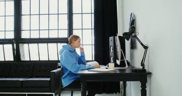 Eine junge Frau in Freizeitkleidung benutzt einen Computer, während sie von zu Hause aus arbeitet — Stockvideo