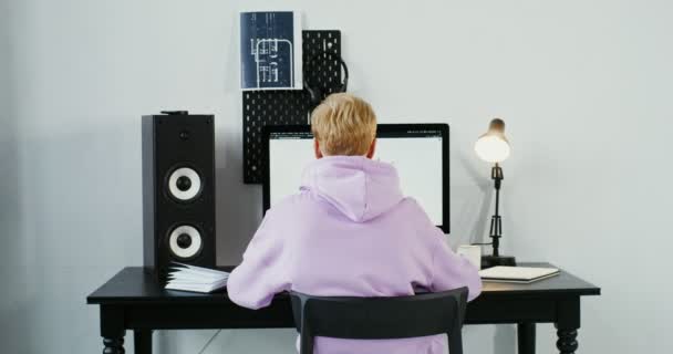 Ένας νεαρός άνδρας με καθημερινά ρούχα χρησιμοποιεί έναν υπολογιστή, που δουλεύει εξ αποστάσεως από το σπίτι. — Αρχείο Βίντεο