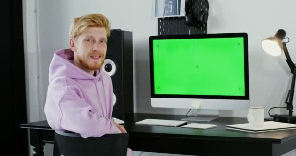 Ένας νεαρός άνδρας με καθημερινά ρούχα, πλησιάζει τον υπολογιστή κάθεται κάτω και αρχίζει να εργάζεται — Αρχείο Βίντεο