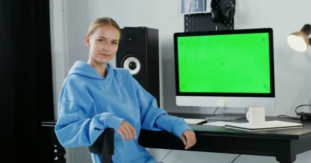年轻女人笑着看着摄像机，坐在一个绿色监视器前 — 图库视频影像