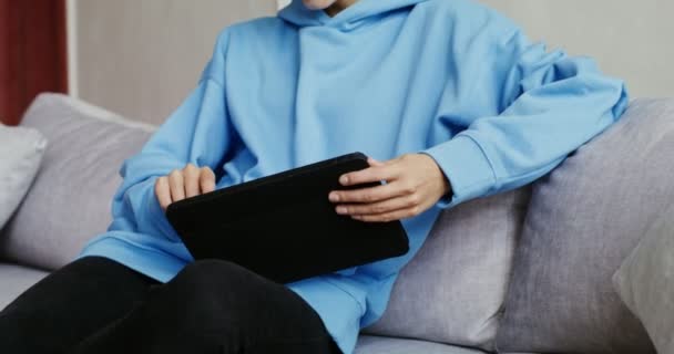 現代的なインテリアのソファに座って、タブレットを使用してカジュアルな服の若い女性 — ストック動画