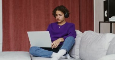 Yakışıklı adam video görüşmesinde konuşuyor. Kanepede dizüstü bilgisayarla oturuyor.