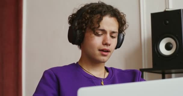Bello ragazzo in abiti casual e cuffie utilizza laptop godendo e cantando — Video Stock