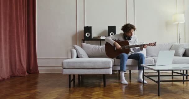 En kille som tittar på gitarr tutorial på laptop och lär sig spela instrument — Stockvideo