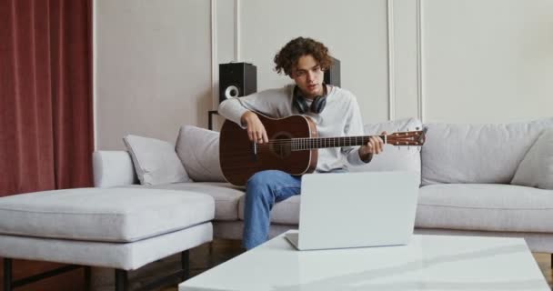 Un tipo viendo tutorial de guitarra en el portátil y aprendiendo a tocar el instrumento — Vídeos de Stock