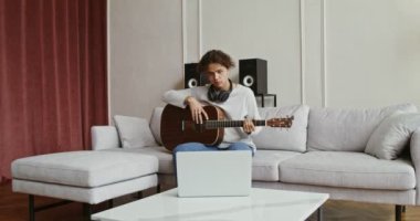 Dizüstü bilgisayarda gitar dersi izleyen ve enstrüman çalmayı öğrenen bir adam.