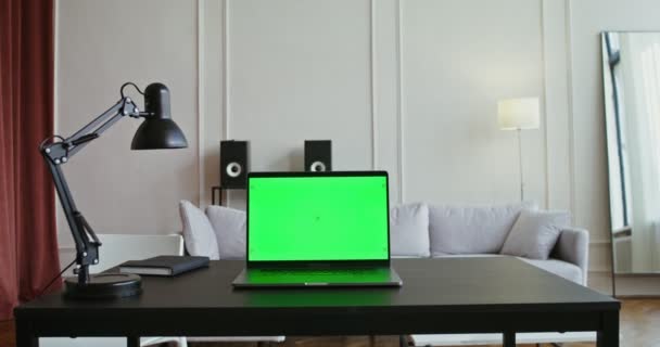 Ένα φορητό υπολογιστή με πράσινη οθόνη κάθεται σε ένα τραπέζι σε ένα σύγχρονο φωτεινό εσωτερικό — Αρχείο Βίντεο