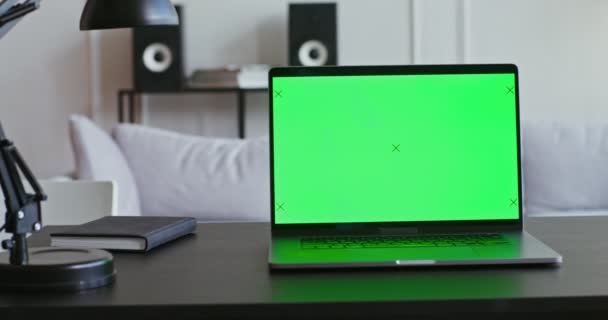 Un ordinateur portable avec un écran vert est assis sur une table dans un intérieur moderne et lumineux — Video