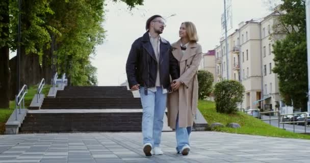 Elegante chico y chica están caminando por la ciudad, tomados de la mano y hablando — Vídeo de stock