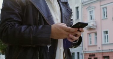 Genç bir adam sonbahar şehrinin caddesinde yürürken telefonu kullanır.