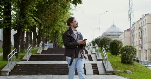 Un jeune homme utilise le téléphone tout en se promenant dans la rue de la ville d'automne — Video