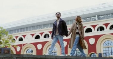 Genç çift merdivenlerden inip el ele tutuşur, konuşur ve güler.