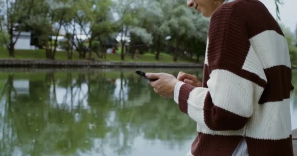 Krásná žena se usmívá při používání mobilního telefonu, sedí na nábřeží — Stock video