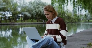 Genç bir kız kaldırımda dizüstü bilgisayar kullanıyor.