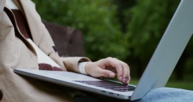 Genç bir kadın dizüstü bilgisayarda çalışıyor, bankta oturuyor ve kahve içiyor.