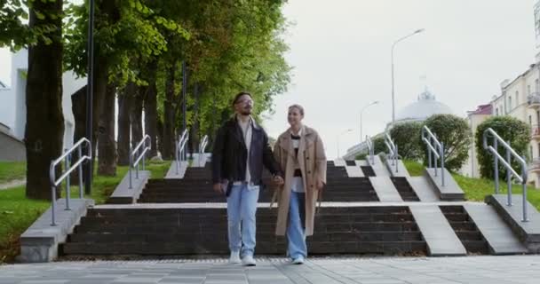 Стильные парень и девушка ходят по городу, держась за руки и разговаривая — стоковое видео