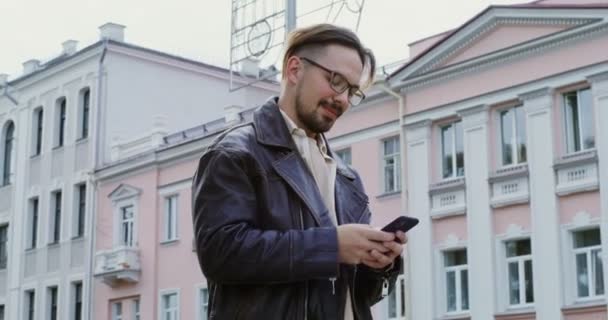 Um jovem usa o telefone enquanto caminha pela rua da cidade do outono — Vídeo de Stock