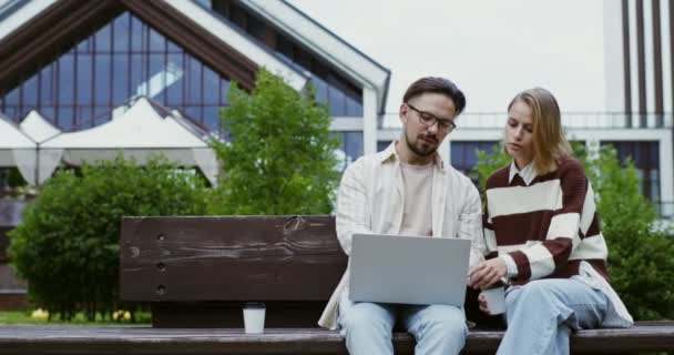 Une femme s'approche d'un gars qui travaille sur un ordinateur portable assis sur un banc et le salue — Video