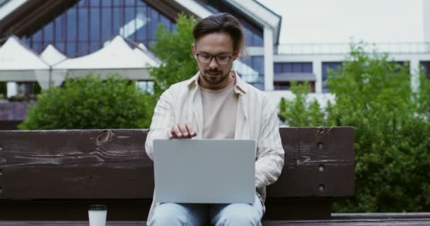 Een jongeman komt, zit op een bank, opent zijn laptop en begint te werken. — Stockvideo