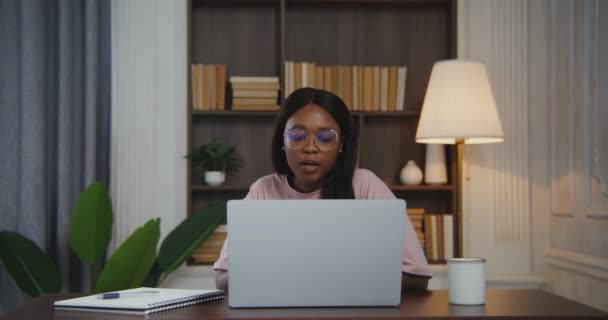 Африканская американка разговаривает в видеочате на ноутбуке, сидя за столом — стоковое видео