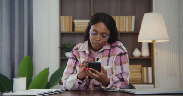 アフリカ系アメリカ人の女性は、現代的なインテリアの机に座っている間に電話を使用します — ストック動画