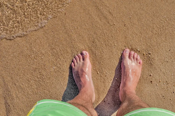 Homem pernas na praia de areia e ondas do mar ao pôr do sol — Fotografia de Stock