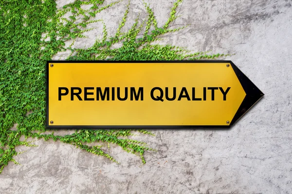 Premium-Qualität auf gelbem Schild an Efeu-Wand — Stockfoto