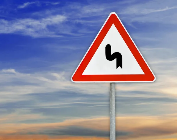 Trójkąt drogowy znak lewo krzywej na pręt z pochmurnego nieba — Zdjęcie stockowe