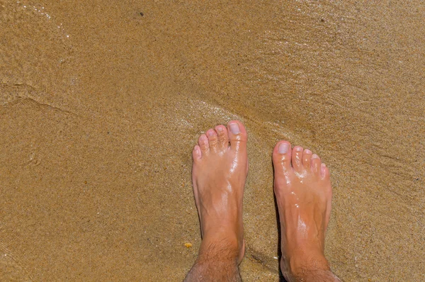 Homem fica no mar e olha para o pé na areia e na água — Fotografia de Stock