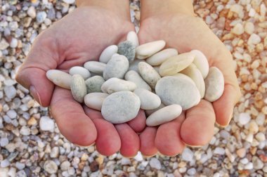 Eller kadın plaj arka plan üzerinde elinde tutan küçük taşlarla güneş yanan sarı ile