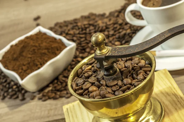 Moedor de café com grãos de café, xícara de café e café moído em tigela na mesa de madeira — Fotografia de Stock