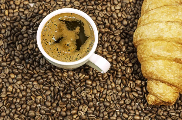 Fundo de grão de café com xícara de café quente fresco e croissant na mesa da cozinha — Fotografia de Stock