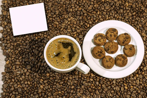 Fundo de grão de café com xícara de café quente fresco e prato cheio de cookies com chocolate e amostra de texto na mesa da cozinha — Fotografia de Stock
