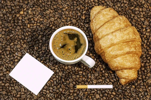 Fundo de grão de café com xícara de café quente fresco, charuto e croissant com espaço para texto na mesa da cozinha — Fotografia de Stock