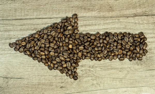 Grãos de café na forma de setas sobre fundo de madeira — Fotografia de Stock