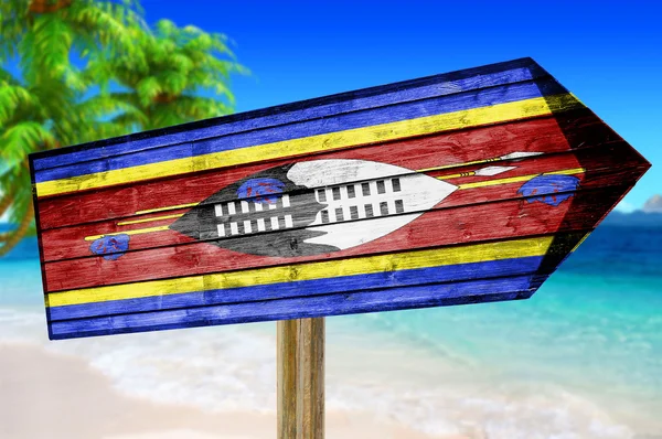 Cartel de madera con bandera de Suazilandia sobre fondo de playa — Foto de Stock