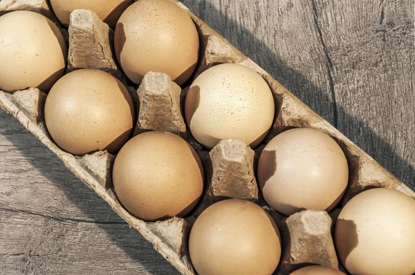 Ten brown eggs in a carton package on a wooden table, eggs on ta