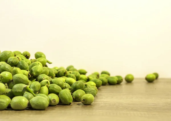 Veel groene jonge walnoten in bolsters op bruin houten keuken tabel en witte achtergrond — Stockfoto